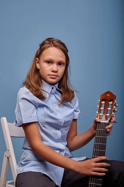 11 yaşında güzel bir kız, mavi arka planda gitarda bir melodi prova ediyor.