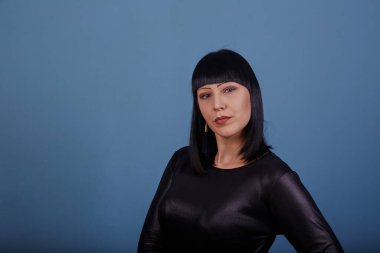 Siyah elbiseli siyah saçlı güzel bir kız, koyu bir arka planda erotik pozlar veriyor.