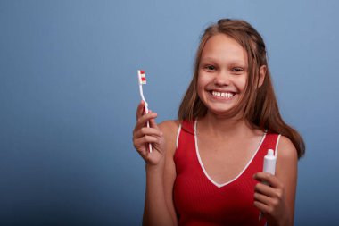 11 yaşında neşeli, güzel bir kız dişlerini mavi bir arka planda fırçalıyor.