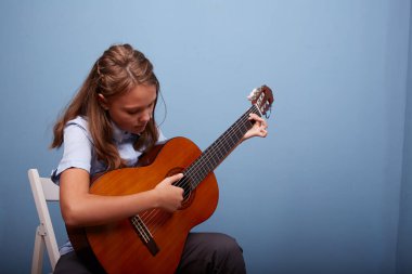 11 yaşında güzel bir kız, mavi arka planda gitarda bir melodi prova ediyor.