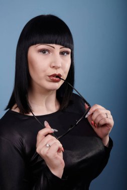 Stüdyoda bir fotoğrafçıya mavi arka planda poz veren gözlüklü güzel bir kızın portresi