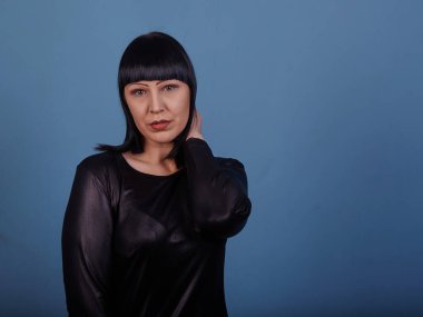 Siyah elbiseli siyah saçlı güzel bir kız, koyu bir arka planda erotik pozlar veriyor.