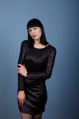 Siyah elbiseli siyah saçlı güzel bir kız, koyu bir arka planda erotik pozlar veriyor.