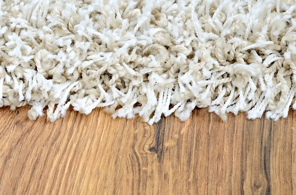 Close-up of white shaggy carpet on brown wooden floor — Stock Photo, Image