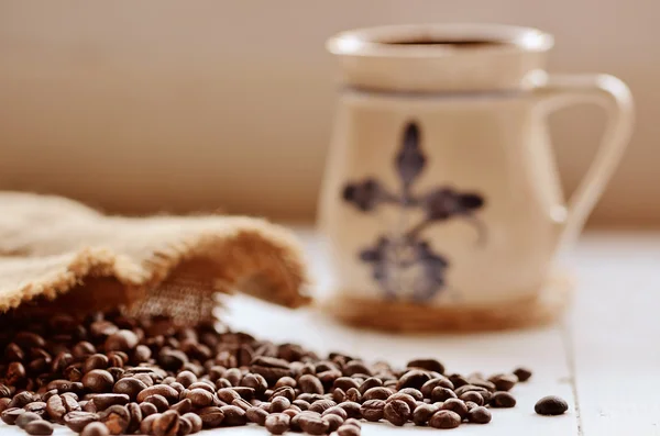 Spilled coffee beans from canvas sack and ceramic mug — Stock Photo, Image