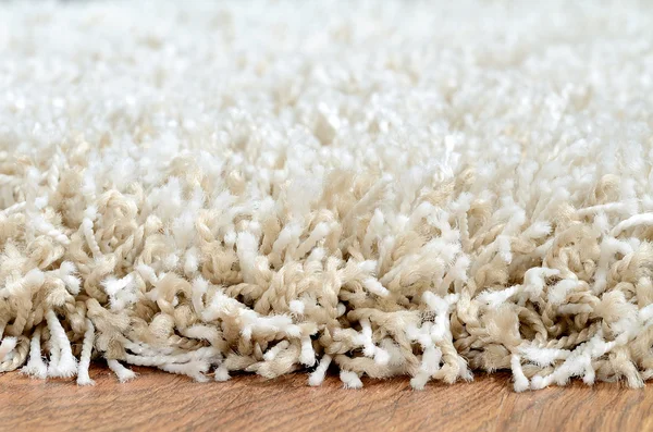 Detail bílých shaggy koberce na hnědé dřevěné podlahy — Stock fotografie