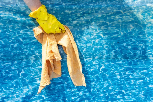 Primer plano de una mano en un guante de goma con trapo mientras se limpia una piscina de jardín. Preparación de la piscina para la temporada de baño de verano —  Fotos de Stock