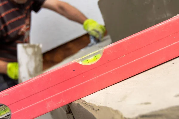 Detail of a spirit level and water bubbles for measuring the flatness of the stair surface when laying paving. Working man with trowel in background. — Foto de Stock