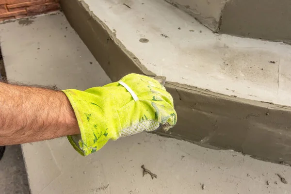 El primer plano de la mano de un hombre en guantes de trabajo nivelando la superficie de un paso antes de la colocación de pavimentación. El hombre limpia el pegamento de mampostería con una espátula — Foto de Stock