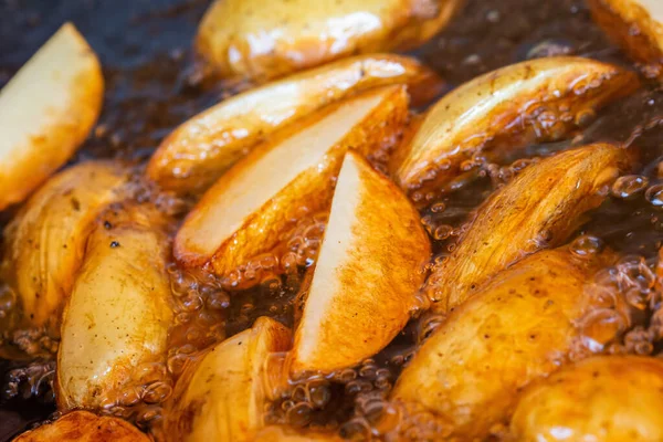 Pedaços cortados de batatas fritas em óleo. Preparação de batatas americanas saborosas para churrasco. Close-up. Imagem De Stock