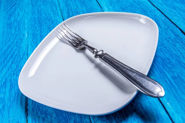 Close-up of empty squared white ceramic plate and silver cutlery on blue wooden boards. Copy space. — Stock Photo, Image