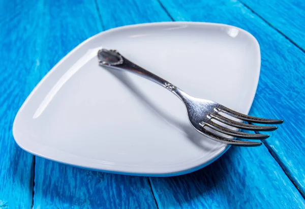 Close-up of empty squared white ceramic plate and silver cutlery on blue wooden boards. Concept cuisine background — Stok fotoğraf