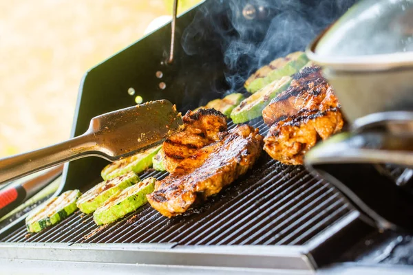 Moderna griglia giardino a gas. Preparazione di succose bistecche di pollo e fette di zucchine alla griglia Immagine Stock