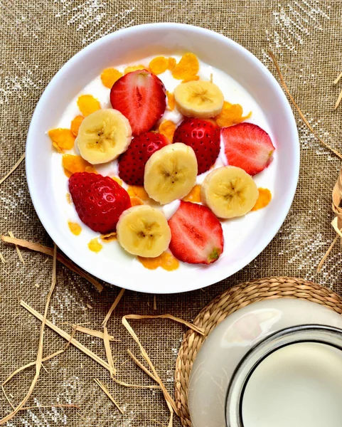 Gesunde Obstschale mit Joghurt, Banane, Erdbeeren und Cornflakes. Glaskrüge mit Kuhmilch vorhanden. Ansicht von oben — Stockfoto