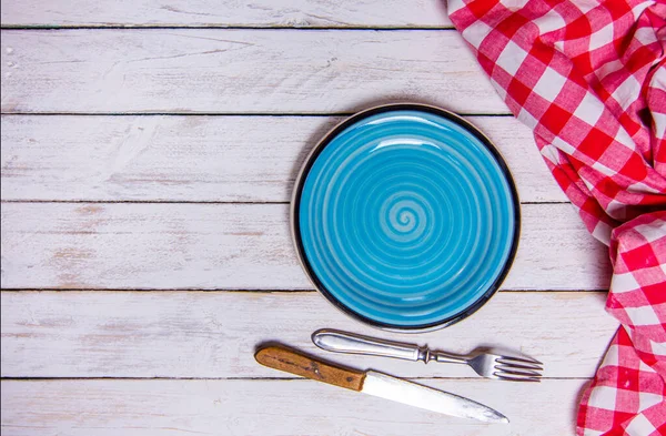 Top view background with empty blue ceramic plate, antique silver cutlery on vintage weathered white wooden boards. Copyspace. Red checkered kitchen towel. — Φωτογραφία Αρχείου