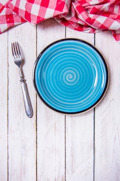 Top view background with empty blue ceramic plate, antique silver cutlery on vintage weathered white wooden boards. Copyspace. Red checkered kitchen towel. Vertical photo. — Φωτογραφία Αρχείου