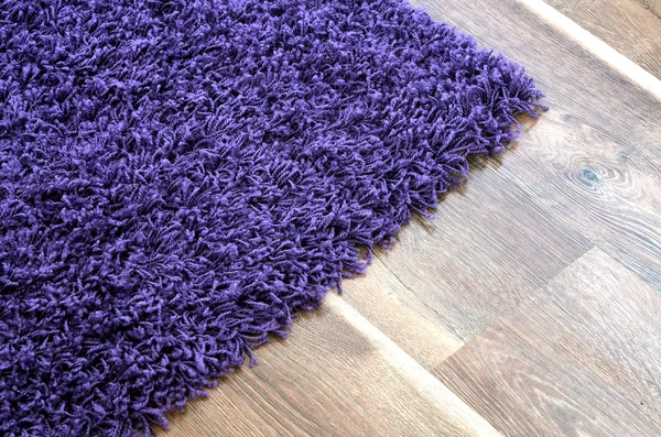 Tappeto shaggy viola sul pavimento in legno marrone — Foto Stock