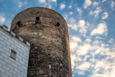 Eski tuğladan güçlendirilmiş bir kuleye bakın ve beyaz cepheli, mavi gökyüzünün önünde akşam ışığında beyaz bulutlar