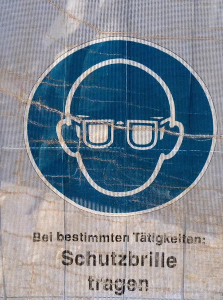 Symbol on a transparent tarpaulin as an indication of safety on a construction site. You can see that you should wear safety goggles. The text means in German: Wear safety goggles.