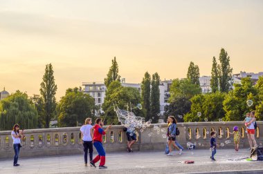 Berlin, Almanya - 17 Haziran 2019: Seyircilerini renkli sabun baloncuklarıyla eğlenceli bir şekilde eğlendiren bir sokak sanatçısı. Berlin 'in merkezindeki bir köprüde hokkabazlık yapıyor..