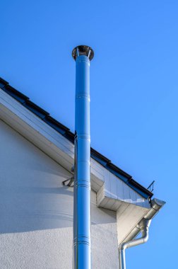 Paslanmaz çelik baca ve parlak mavi gökyüzünün önündeki çatının parçaları..