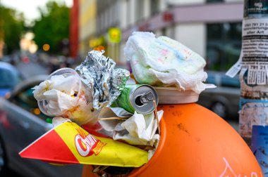 Berlin, Almanya - 28 Haziran 2019: Bir sokak festivali yüzünden yol kenarında aşırı dolu bir çöp kutusu duruyor.