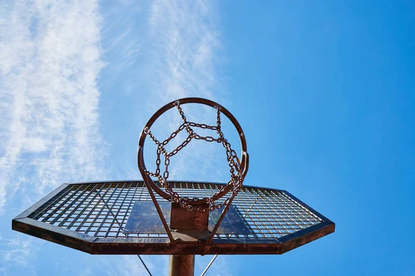 View to a basketball hoop made from chains against a blue sky.
