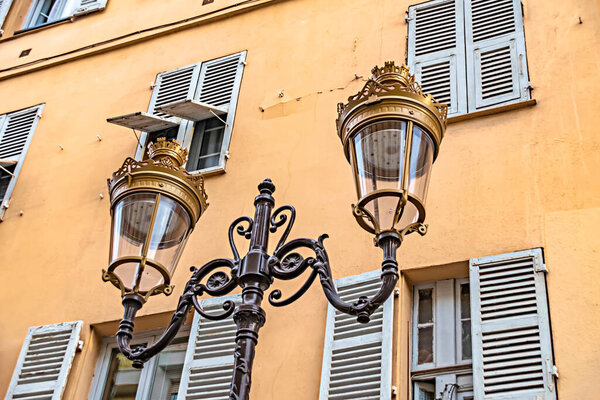 Historic two-armed street lamp in Nice, France, in front of a house facade with wooden shutters.