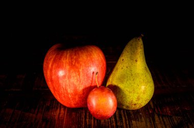 Elma, armut ve erik içeren bir grup taze meyve kırsal bir ahşap masa üzerinde siyah arka planda..