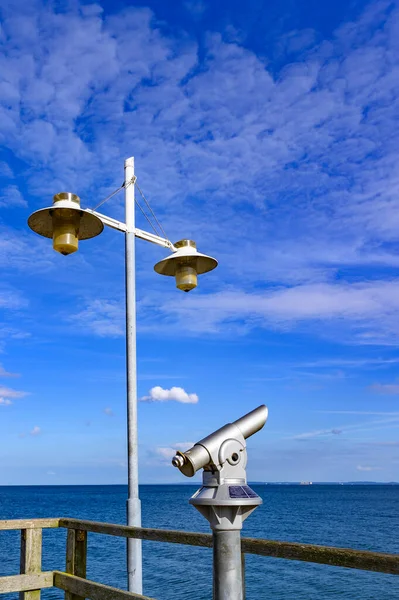 Telescope with coin slot and lantern on the pier in Bansin on the island of Usedom in Germany. Sea and sky are dark blue and radiate in the sunshine.