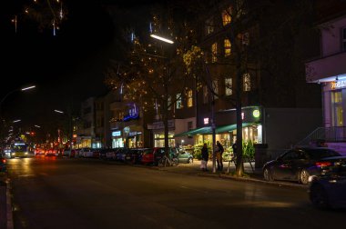 Berlin, Almanya - 12 Aralık 2019: Berlin 'de parlak renkli Noel süslemeleriyle küçük bir alışveriş caddesinin gece sahnesi.