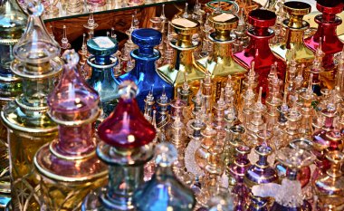 Batan güneşin ışığında camdan yapılmış zengin dekore edilmiş ve renkli parfüm bardakları yan yana dursun. Odak noktası sağ taraftaki büyük flakonlar..