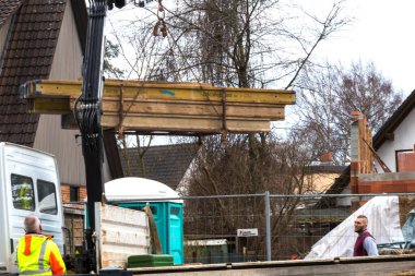 Konut alanındaki bir iş sahasında inşaat malzemelerini kaldıran bir vince bakın. İşçilerden biri vinç kontrollerini kullanırken, diğeri ona bakıyor - Berlin, Almanya - 03 / 13 / 2018