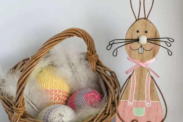 一只带彩绘装饰的木制复活节兔子 在一个有羽毛的柳条篮旁边的铁丝网上 在明亮的背景前 有三个有钩子的蛋 — 图库照片