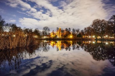 Berlin-Lichtenrade 'da gece lambalarla aydınlatılan tarihi bir köy kilisesi ve bu bir gölete yansıyor..