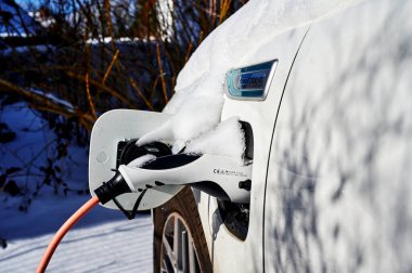 Berlin, Almanya - 12 Şubat 2021: Şarj prizinde kar olan hibrit elektrikli bir araca bakın.