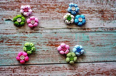 Ortasında bir düğme olan renkli kumaş çiçeklerden yapılmış Paskalya süslemesi, ahşap bir yüzeyde duruyor..