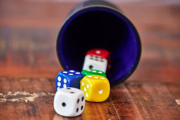 View to different colored game dices and a dice cup on a wooden table.