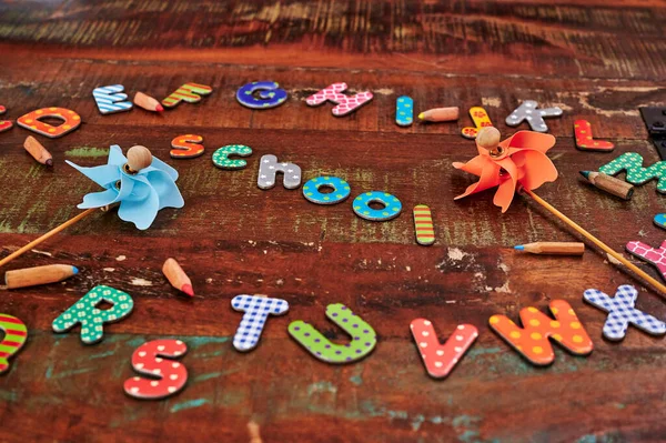 Auburn wooden table with colorful letters that make up the word school and other letters around it.