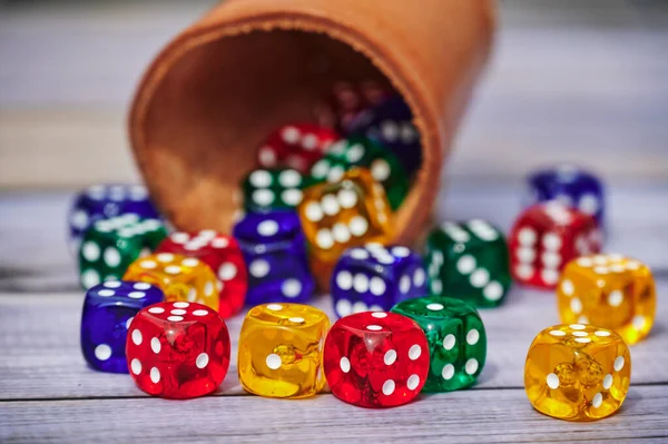 View to different colored game dices and a dice cup on a wooden table.