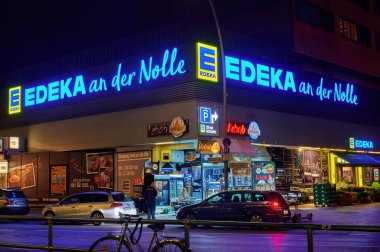 Berlin; Almanya - 23 Haziran 2021: Berlin şehir merkezinde aydınlatılmış bir süpermarketin köşesindeki açık büfenin gece çekimi.