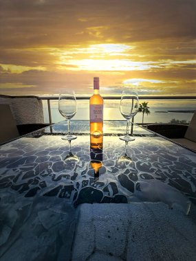 Mallorca, İspanya - 2 Kasım 2025: Bir şarap şişesi ve altın gün batımıyla aydınlanan iki boş bardak.