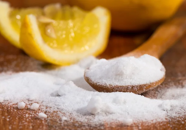 Baking soda (sodium bicarbonate) in a wooden spoon and lemon — Stock Photo, Image