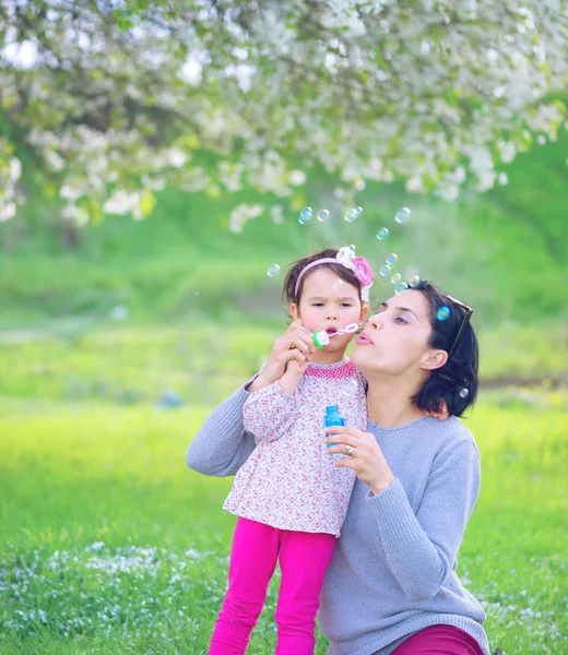 Glückliche junge Mutter und ihre Tochter pusten Seifenblasen im Park — Stockfoto