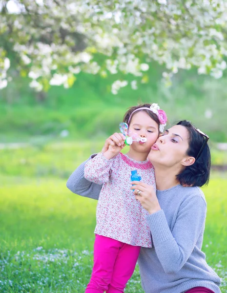 Gelukkig jonge moeder en haar dochter blazen van zeepbellen in park — Stockfoto