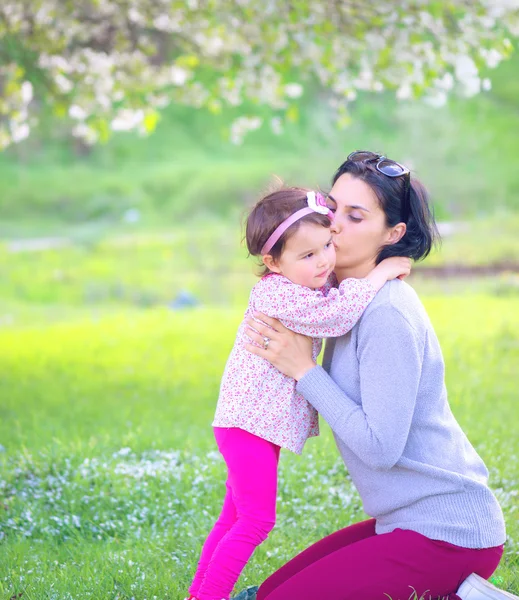 Meisje knuffelen en kussen van haar moeder op groene achtergrond — Stockfoto