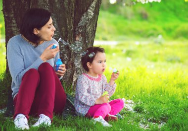 mutlu genç anne ve kızı parkta sabun köpüğü üfleme