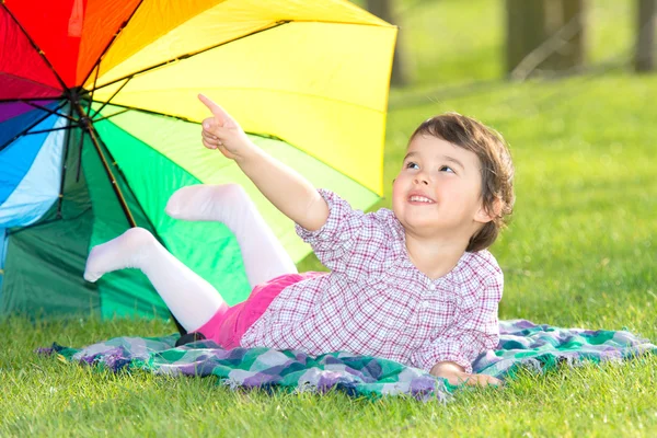 Pequena menina feliz com um guarda-chuva arco-íris no parque — Fotografia de Stock