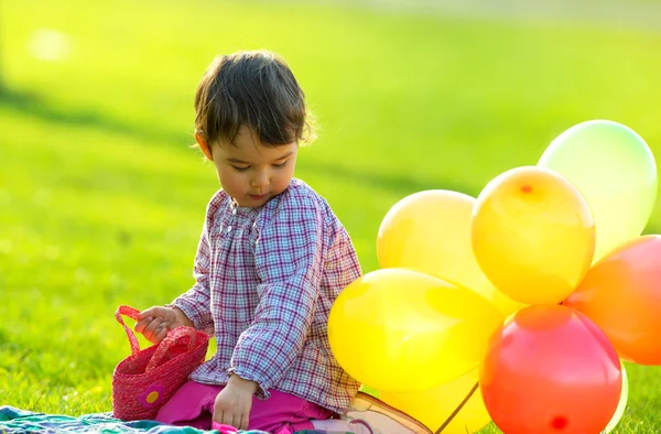 Ittle flicka sitter på gräset med ballonger — Stockfoto