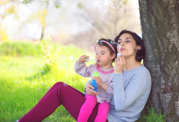 Glückliche junge Mutter und ihre Tochter pusten Seifenblasen im Park — Stockfoto